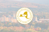 A gold and white seal for the City of Cortland, New York, featuring a map of the state, a crown, and text “The Crown City over a faded cityscape with autumn trees in the background.